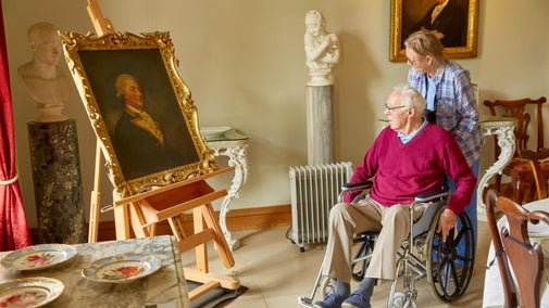 Two visitors admiring a large painting in the house at Melford Hall, Suffolk
